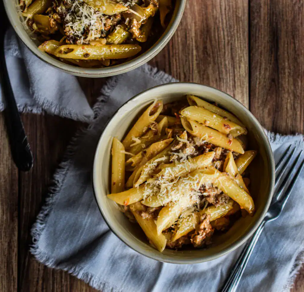 Two bowls of pasta with ground sausage and cheese.