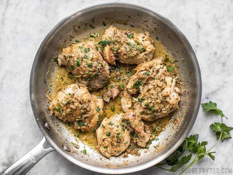 Chicken breasts in a skillet with herbs.