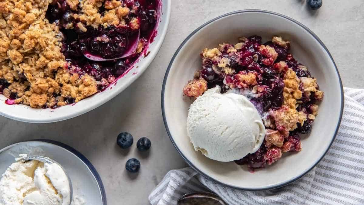 A bowl of blueberry crisp with ice cream and a scoop of ice cream.