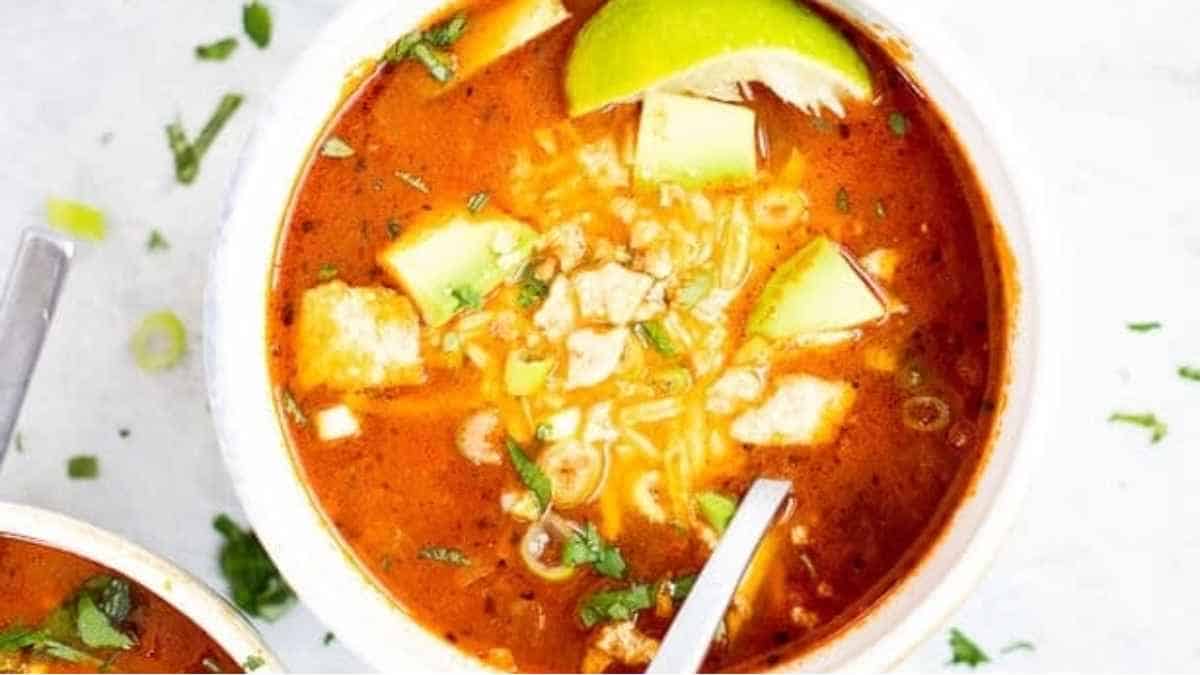 A bowl of mexican chicken soup with avocado and lime.