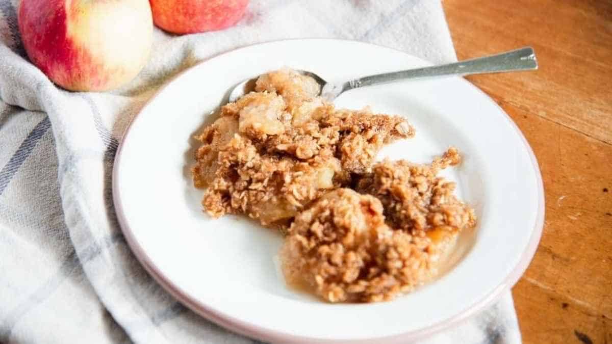 Apple crisp on a white plate with apples next to it.