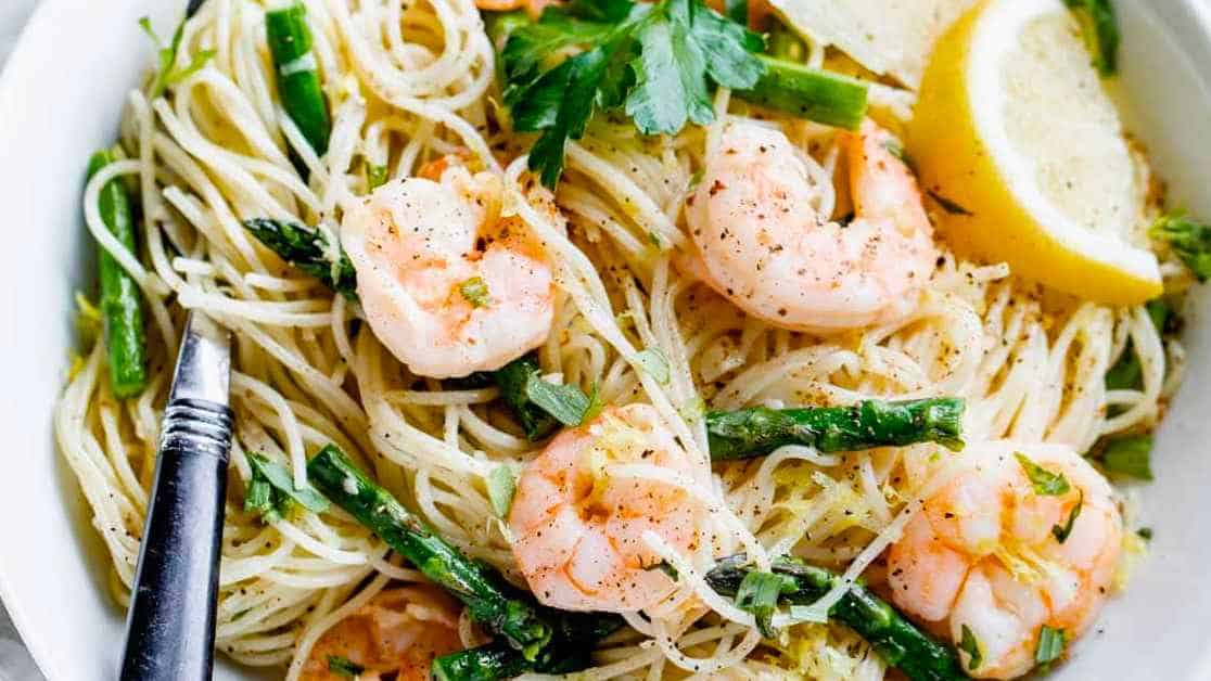 A bowl of pasta with shrimp and lemon wedges.