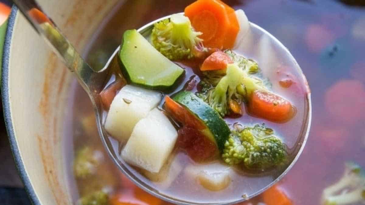 A spoon full of vegetable soup with vegetables in it.
