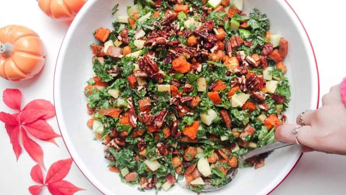 A bowl of kale salad with carrots and pecans.