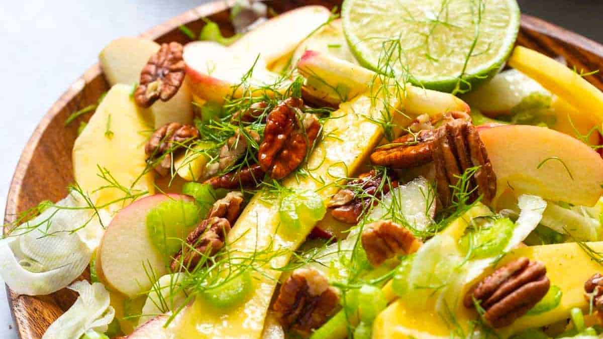 A bowl of mango salad with pecans, apples and limes.