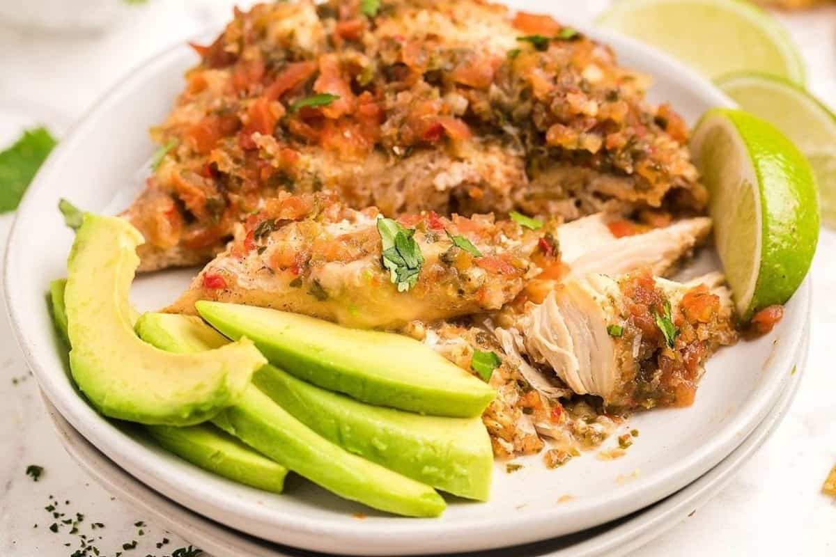 Mexican chicken on a white plate with avocado and lime wedges.