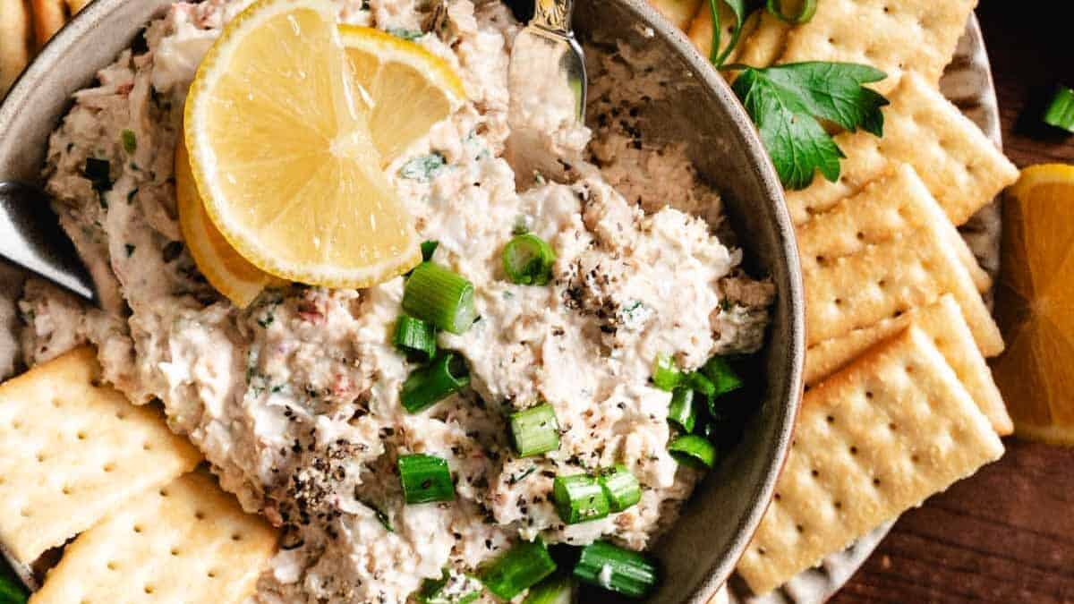 A bowl of tuna dip with crackers and lemon.