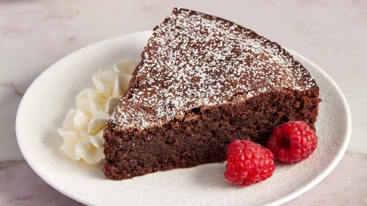 A slice of chocolate cake on a plate with raspberries.