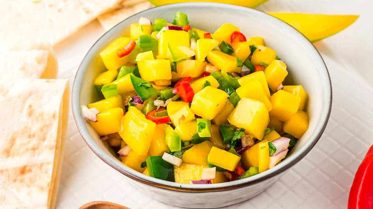 A bowl of mango salsa on a white table.