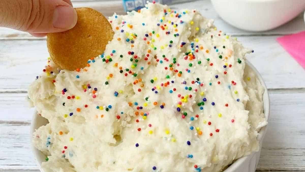 A person is dipping a cookie into a bowl of icing.