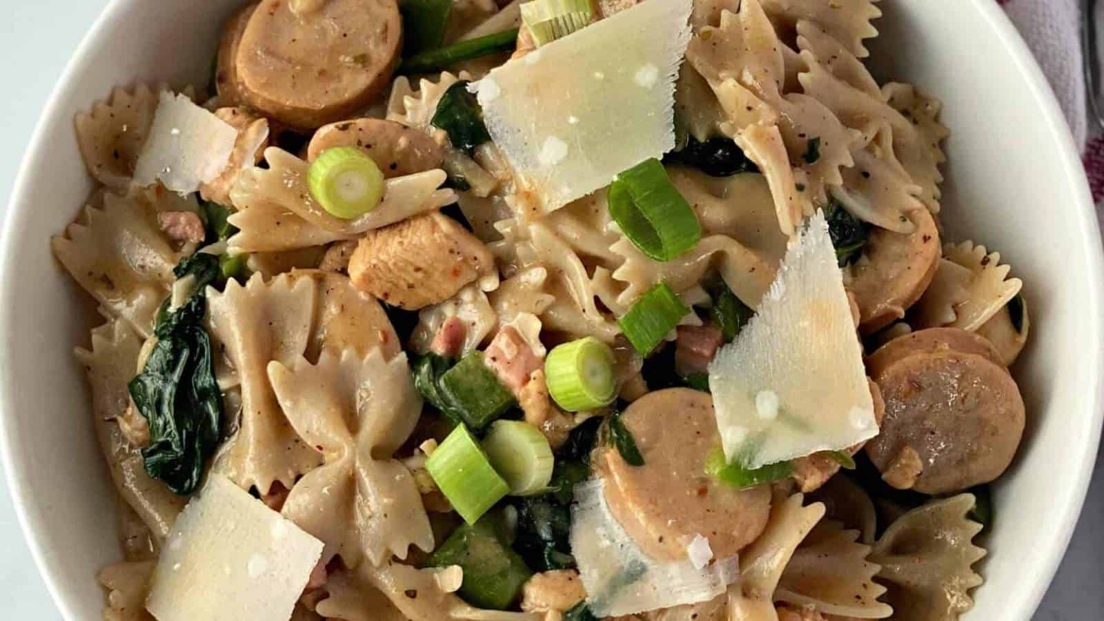 A bowl of pasta with sausage and greens.