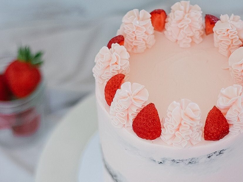 A pink and white cake with strawberries on top.
