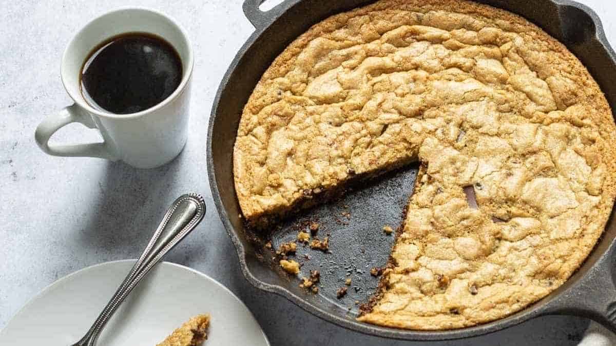 A skillet with a piece of cookie cake and a cup of coffee.