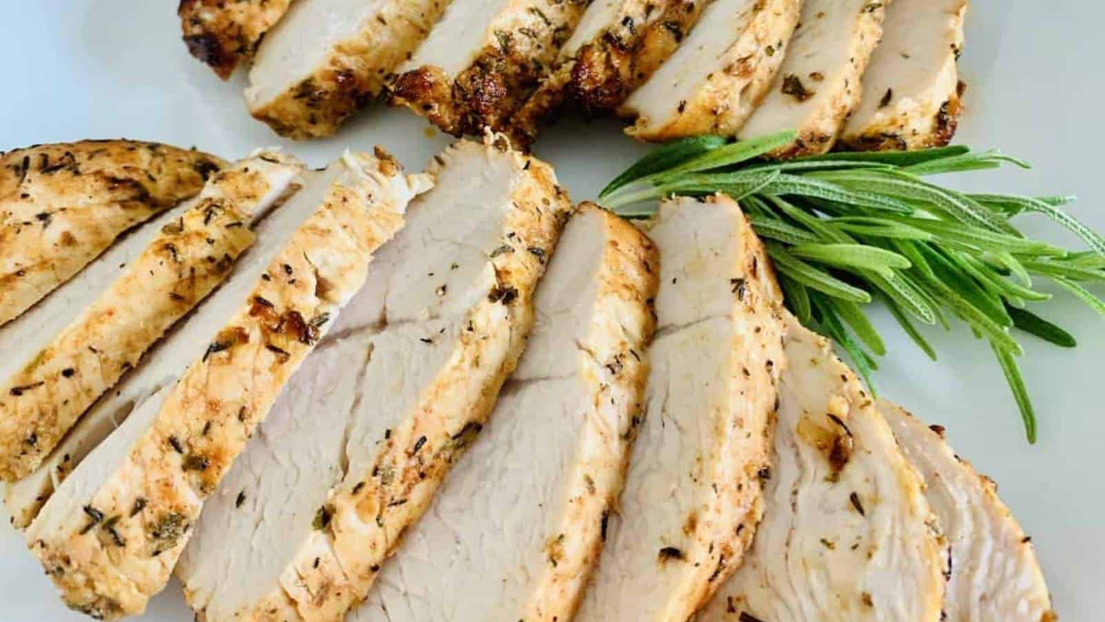 Sliced grilled chicken with rosemary sprigs on a white plate.
