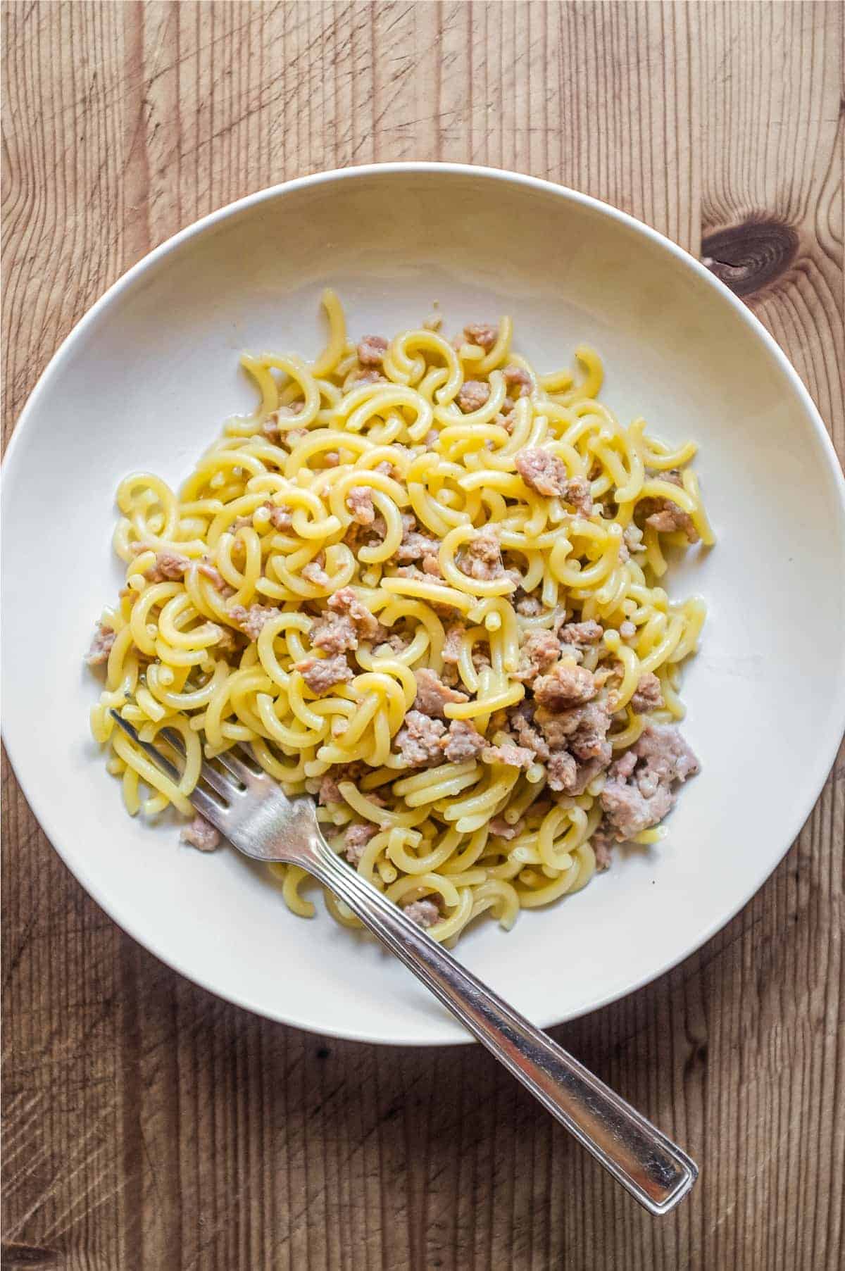 A bowl of noodles with meat and a fork, featuring a delicious ground sausage topping.