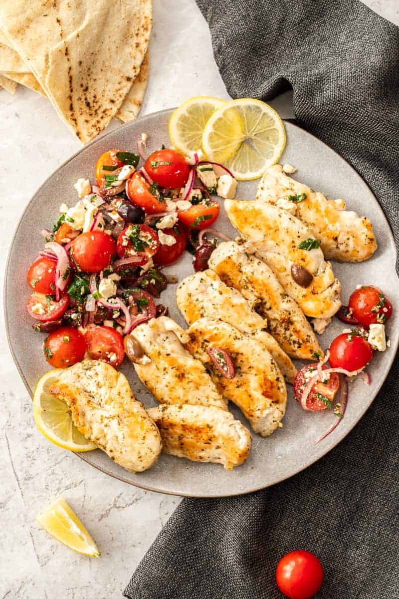 Grilled chicken skewers with tomatoes and lemons on a plate.
