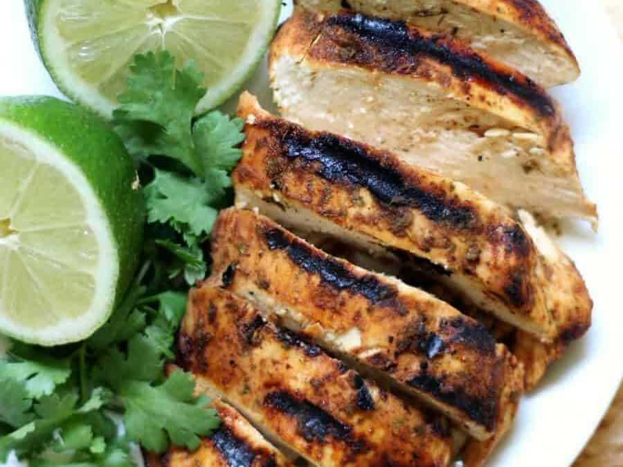 Grilled chicken on a white plate with lime wedges.