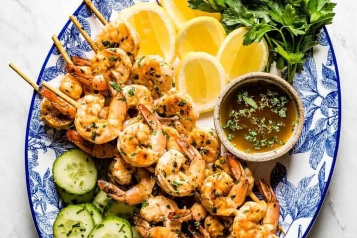 Shrimp skewers on a plate with lemons and cucumbers.