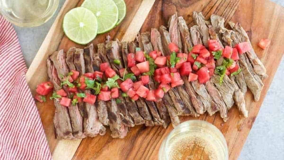 Steak on a cutting board with tomatoes and limes.