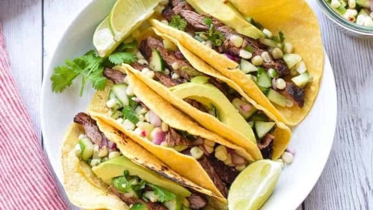 Steak tacos on a white plate with lime wedges.
