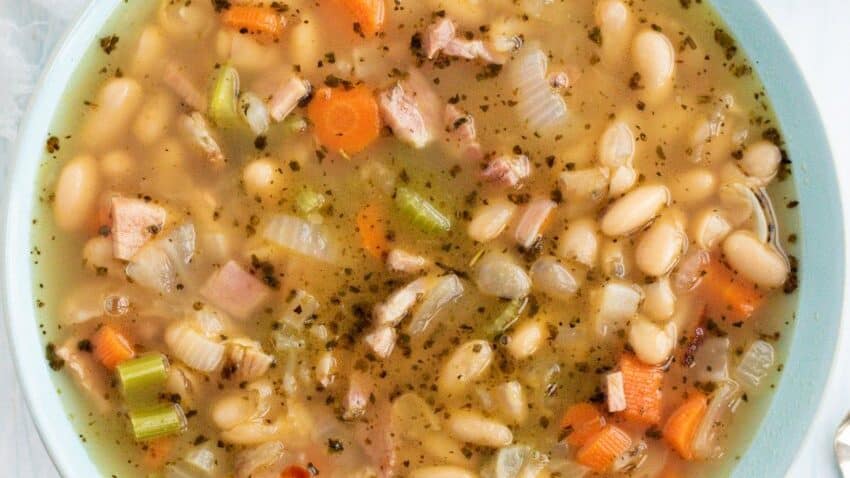 A bowl of white bean soup with ham and carrots.