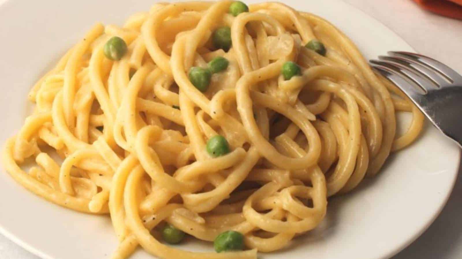 A plate of pasta with peas and a fork.