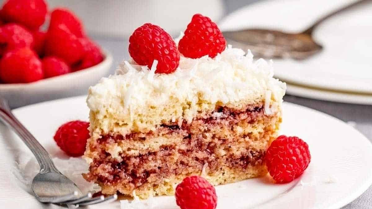 A slice of cake with raspberries and coconut on a plate.