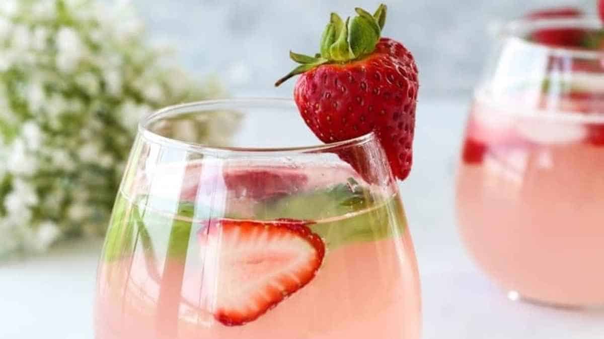 Two glasses of pink sangria with strawberries in them.