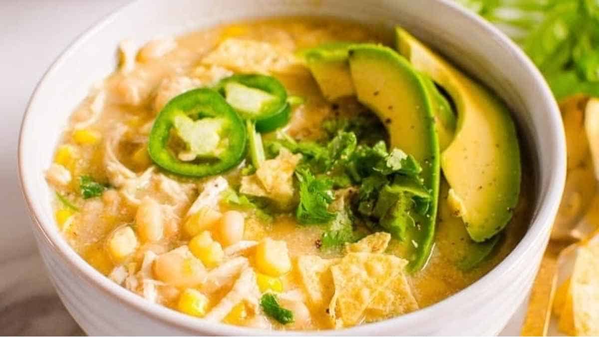 A bowl of chicken enchilada soup with avocado and tortilla chips.