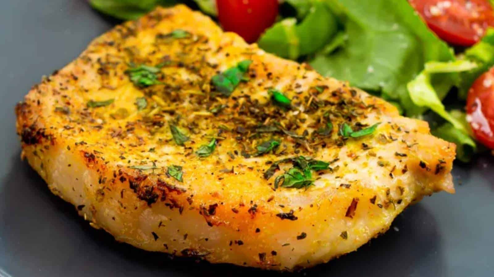 A piece of pork chop on a plate with a salad.