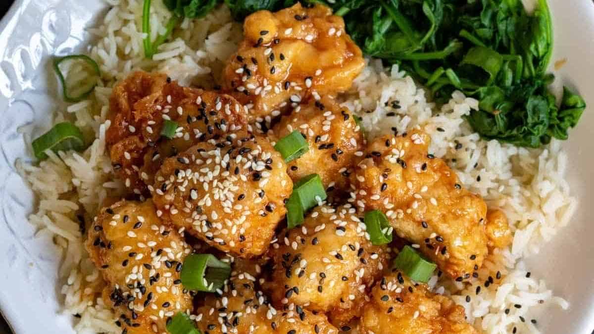 A white plate with sesame chicken and rice.