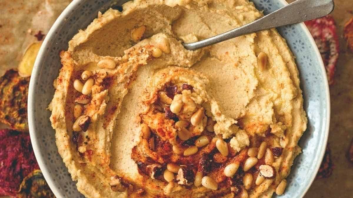 A bowl of hummus with nuts and a spoon.