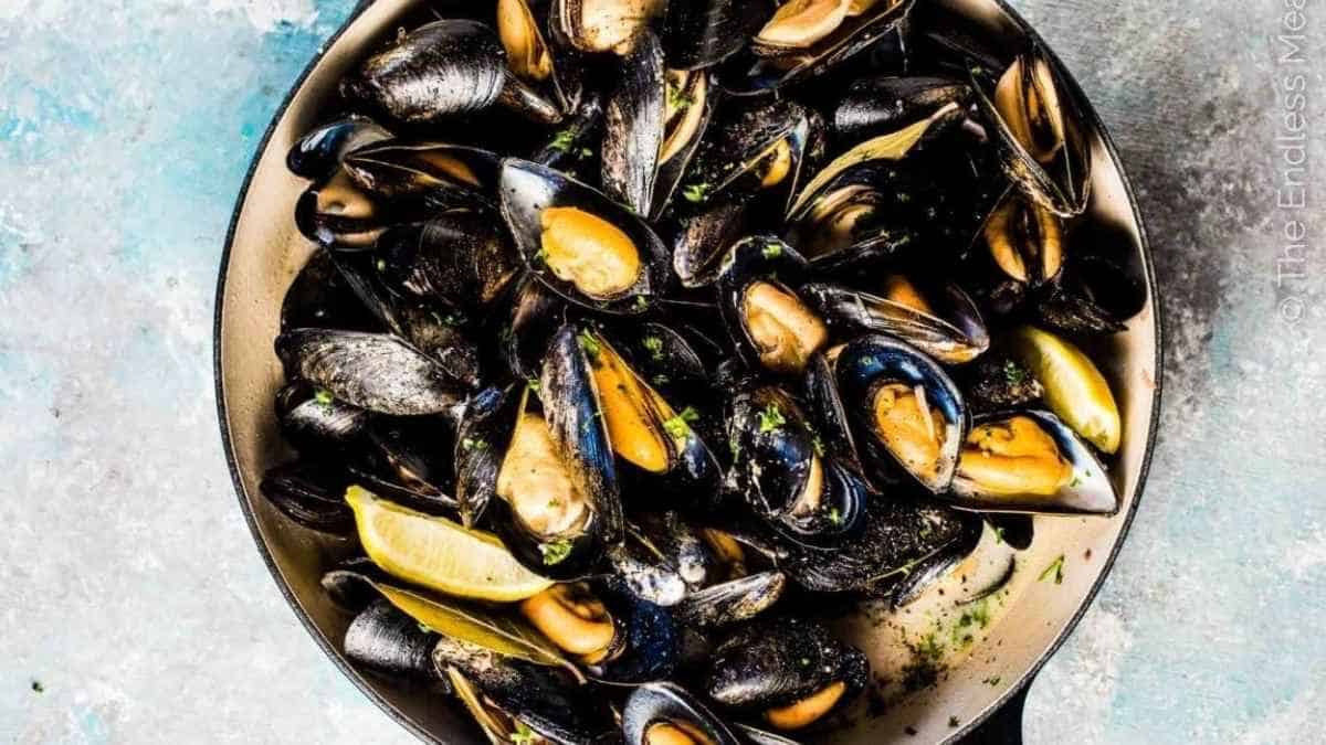 Mussels in a pan with lemon wedges.