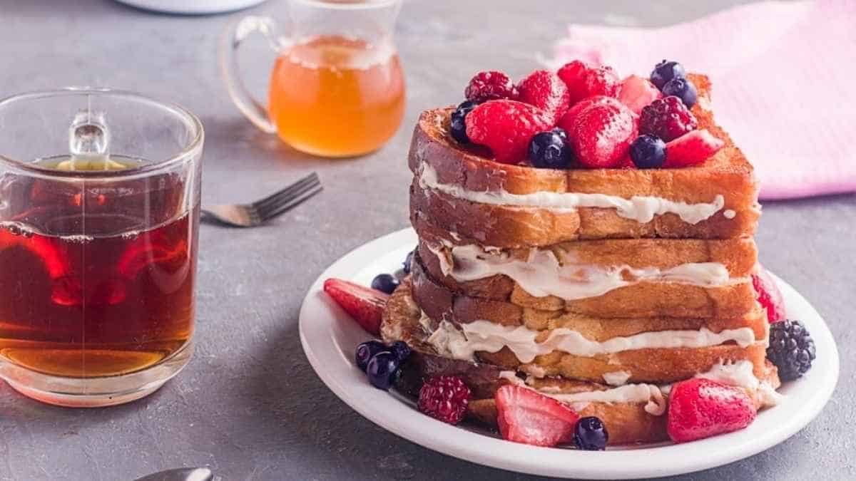A stack of french toast with berries and a cup of tea.