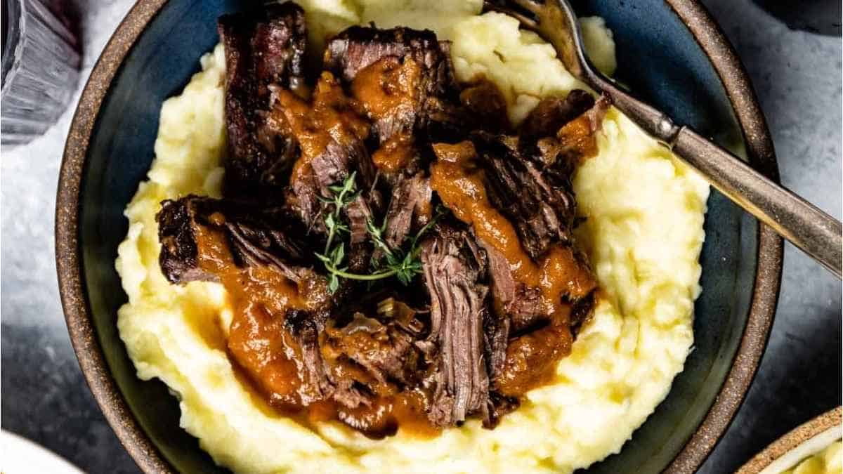 A bowl of beef stew with gravy and mashed potatoes.
