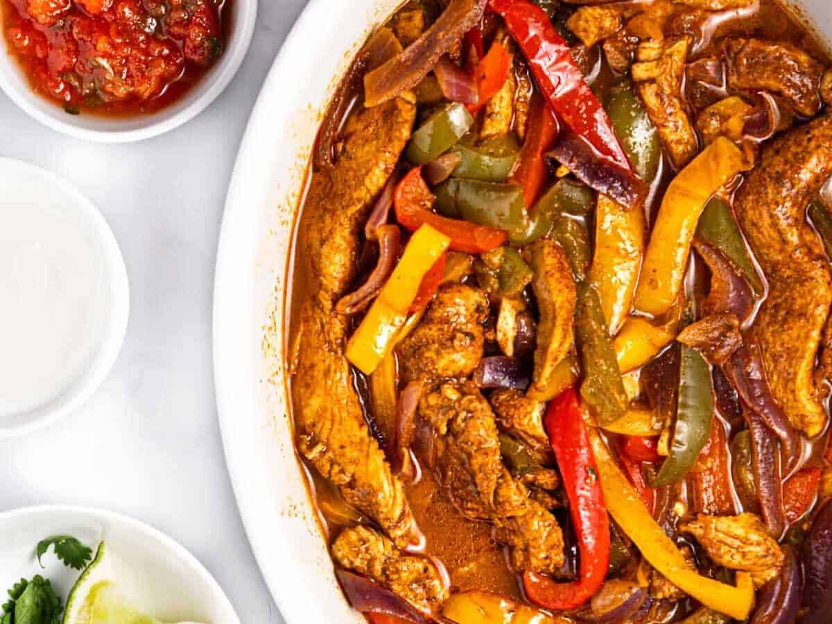 Chicken fajitas in a white bowl with peppers and sauce.