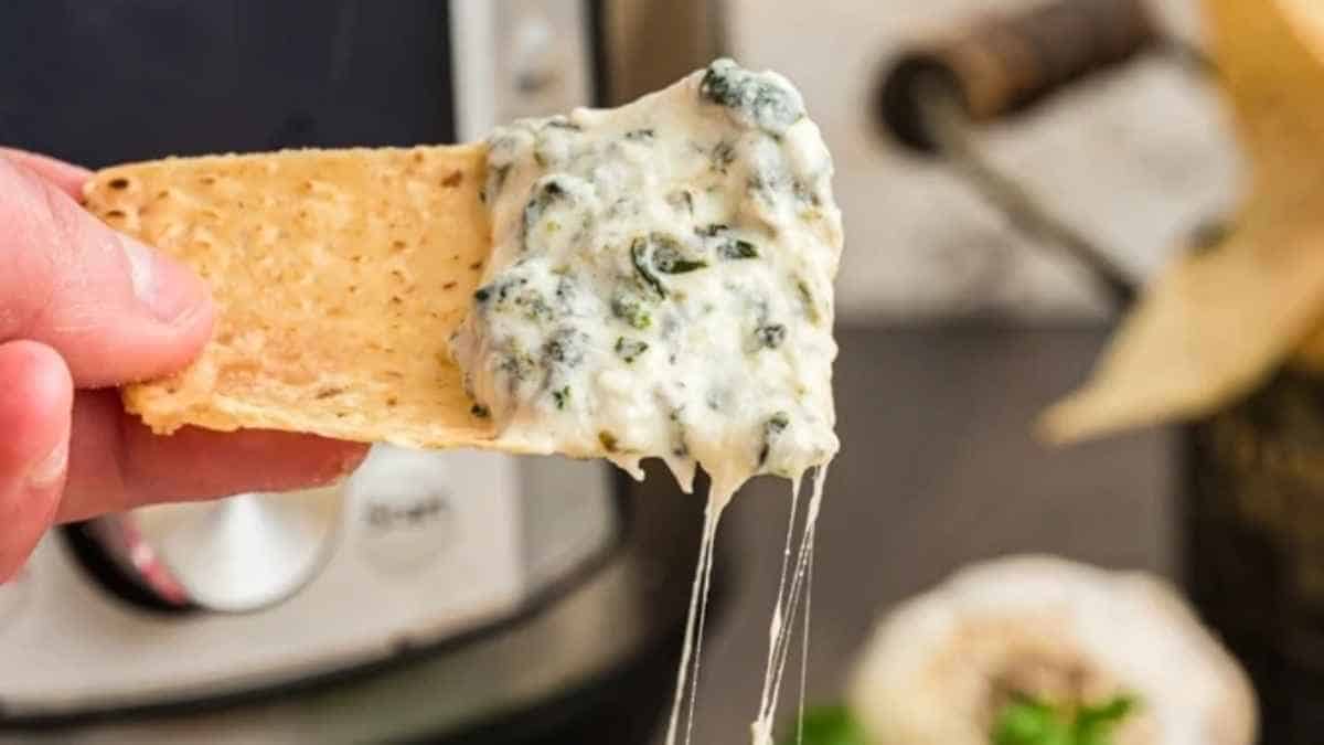 A person dipping a cracker into a bowl of spinach dip.