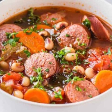 A bowl of soup with sausage, beans and carrots.