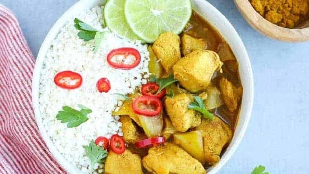 A bowl of chicken curry with rice and lime wedges.