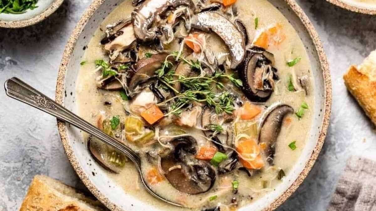 A bowl of mushroom soup with bread on the side.
