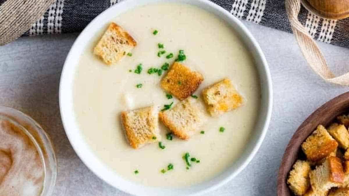A bowl of soup with croutons and bread.