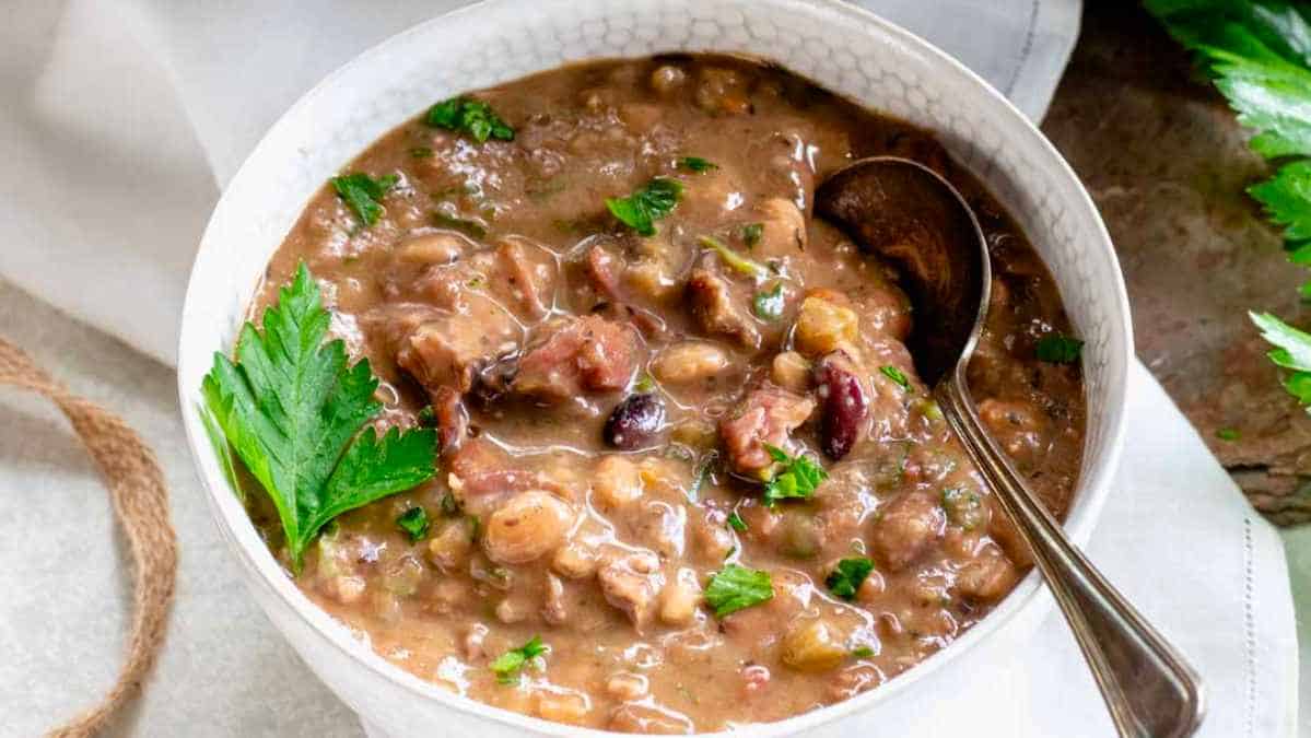 A bowl of bean soup with meat and parsley.