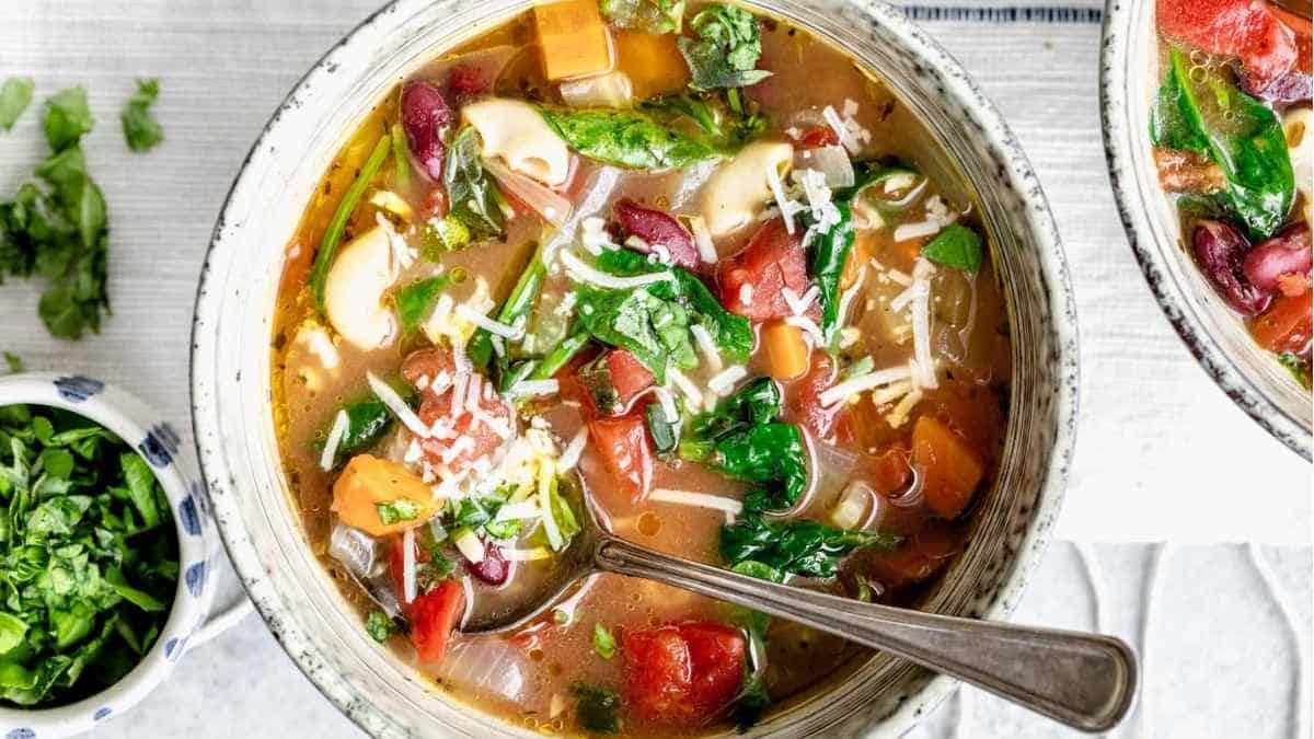 Two bowls of chicken and vegetable soup with a spoon.