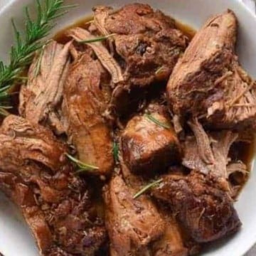 A plate of roasted beef with rosemary sprigs and a fork.