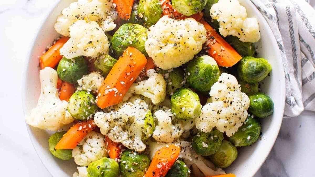 Brussel sprouts, carrots and cauliflower in a white bowl.