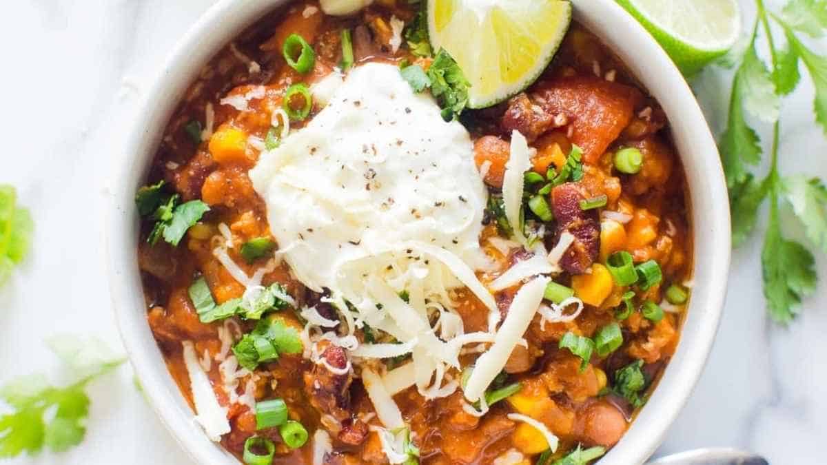 A bowl of mexican bean chili with sour cream and lime.