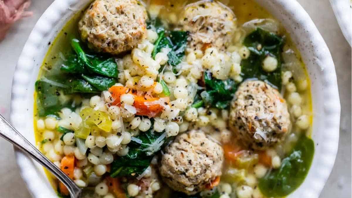 A bowl of soup with meatballs and spinach.