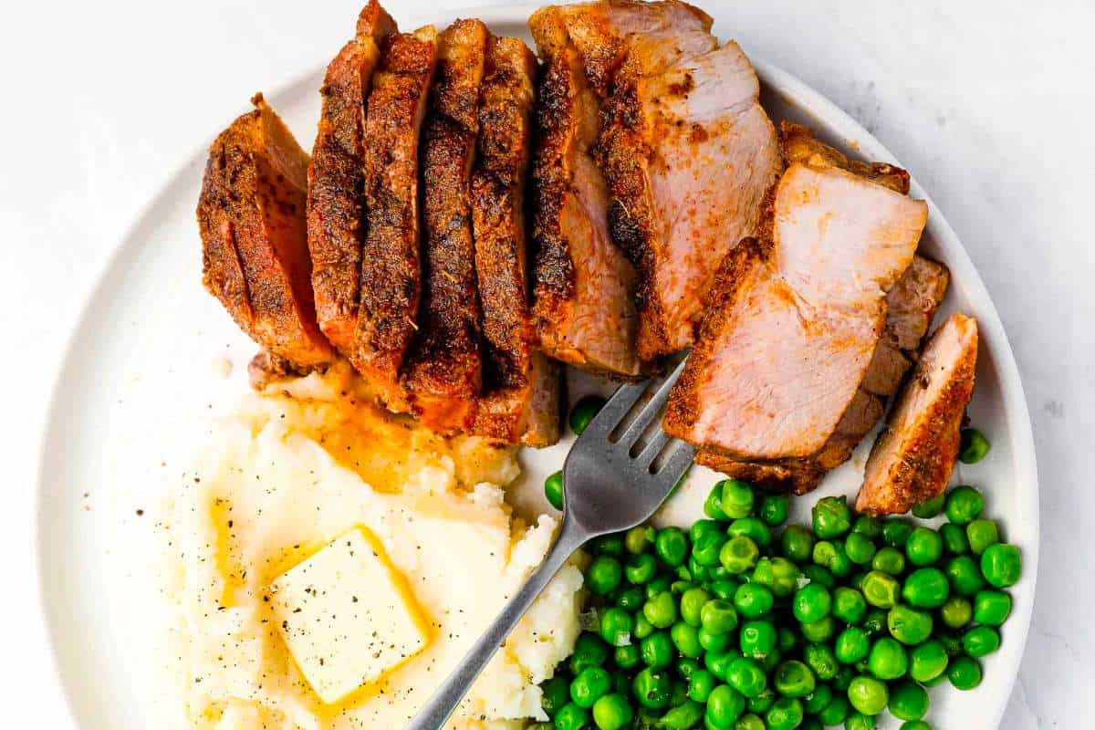 A plate with pork, peas and mashed potatoes.