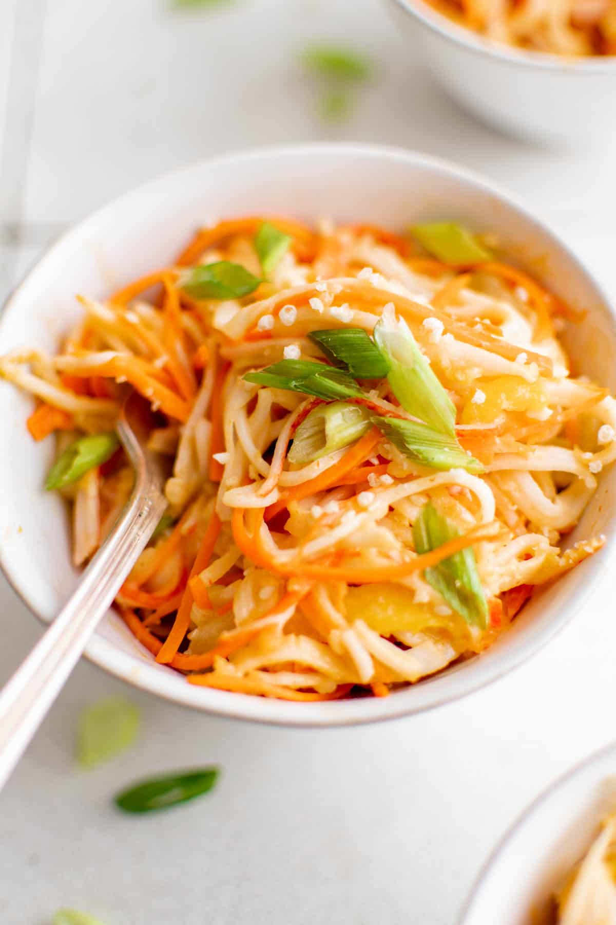 A bowl of noodles with carrots and green onions, served with imitation crab.