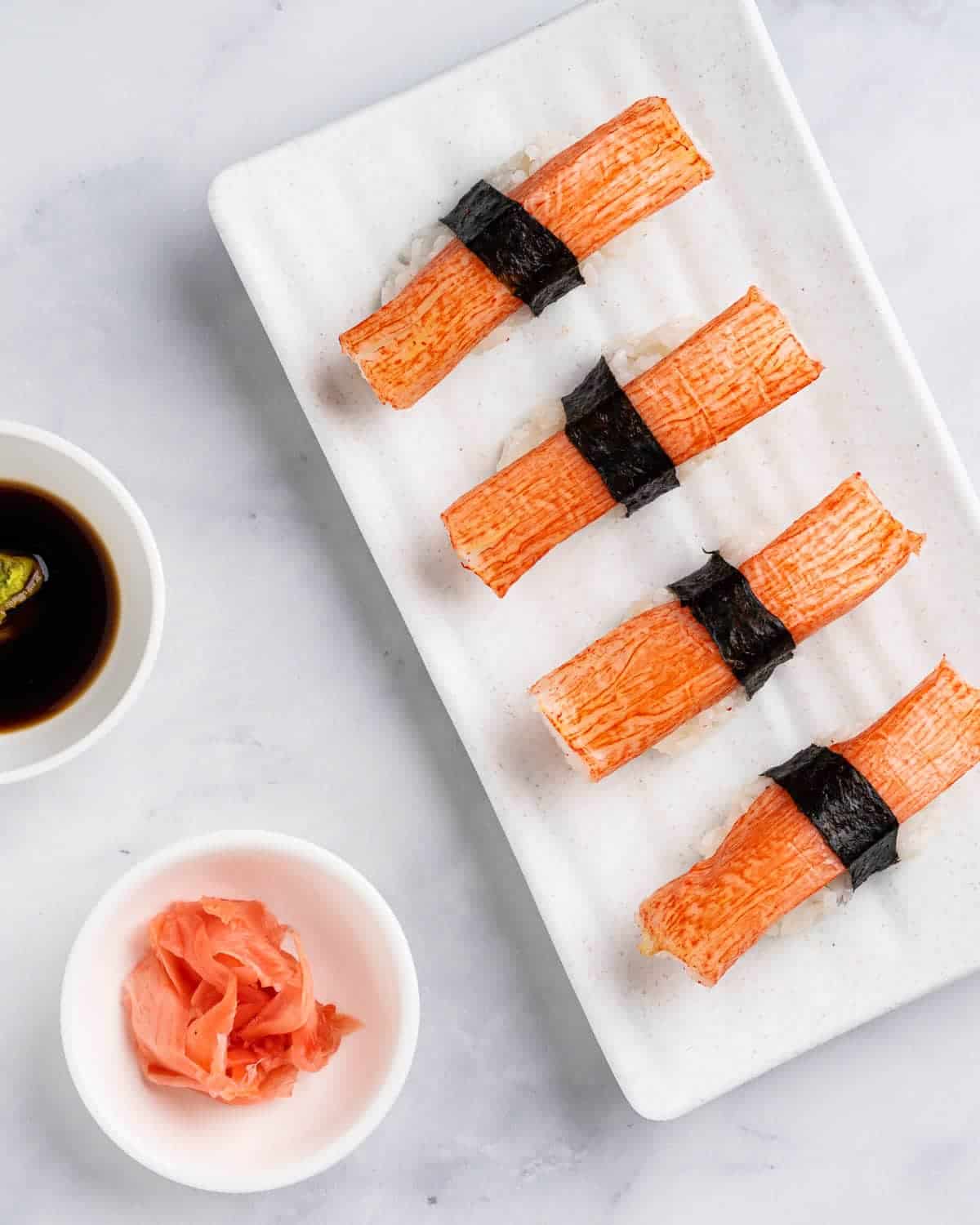 Imitation crab sushi on a white plate with a bowl of sauce.